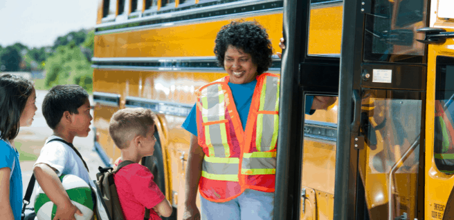 Kids in line to get on a school bus to go back to school with and adult making sure they are safe