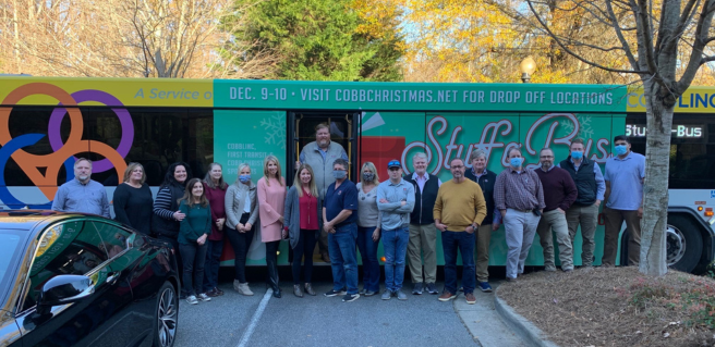 Cobb Christmas 2023 Traton Homes crew standing in front of green stuff a bus