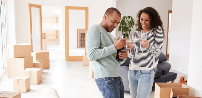 couple moving into home making a champagne toast, surrounded by boxes, modern renter