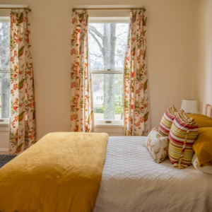 beige guest bedroom with yellow bedding and two large windows